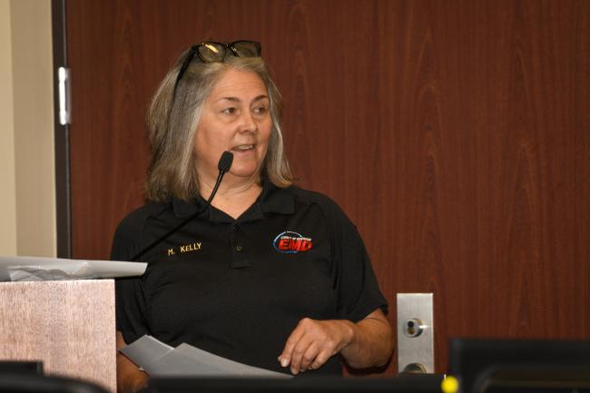 A woman in an EMD polo speaks from a podium at the CERT Field Day.