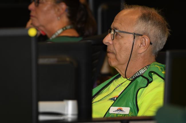 A man in a green CERT vest sits at a desk.