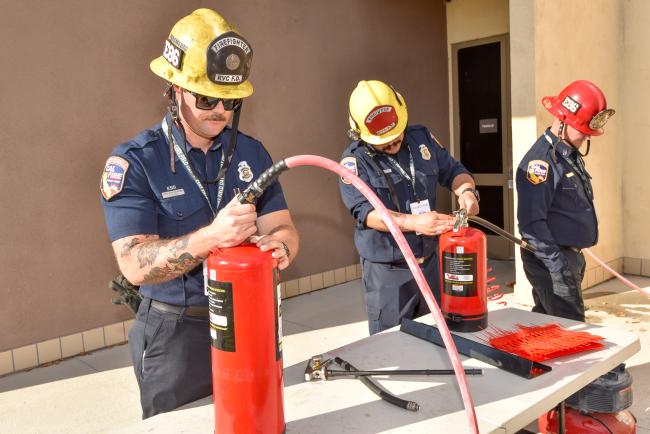 Firefighters fill fire extinguishers with water at a table.