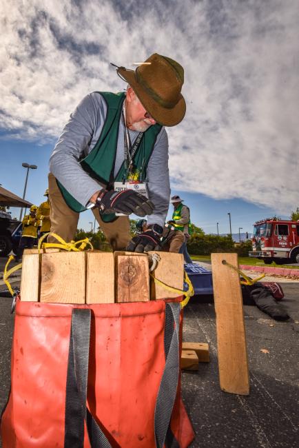 A man in a green CERT vest loads wood blocks into a red bag.