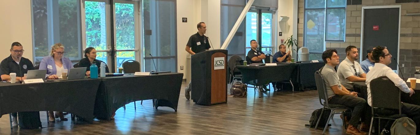 A man stands at a podium while speaking before a room full of workshop attendees.