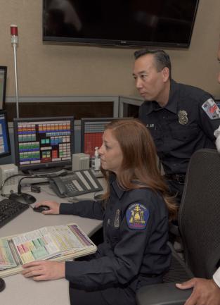 Uniformed personnel from Riverside County Fire, Emergency Management Department and American Medical Response look at a 9-1-1 dispatch terminal.