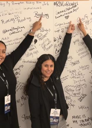 Three women standing and pointing to a wall with a lot of writing. / Tres mujeres de pie y señalando una pared con mucha escritura. 
