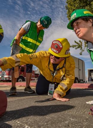 A Firefighter gives direction to a woman in CERT uniform with heavy equipment nearby.
