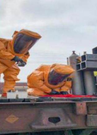 Two hazardous materials technicians, dressed in bright yellow, full body protective suits inspect a hazardous device on a train car during the CHOG drill.